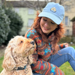 Woman wearing a light blue cap with a dog logo, sitting outdoors with a dog.
