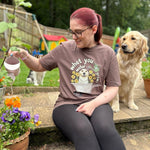 Woman sitting outdoors with a dog, wearing a t-shirt with a graphic design, holding a plant