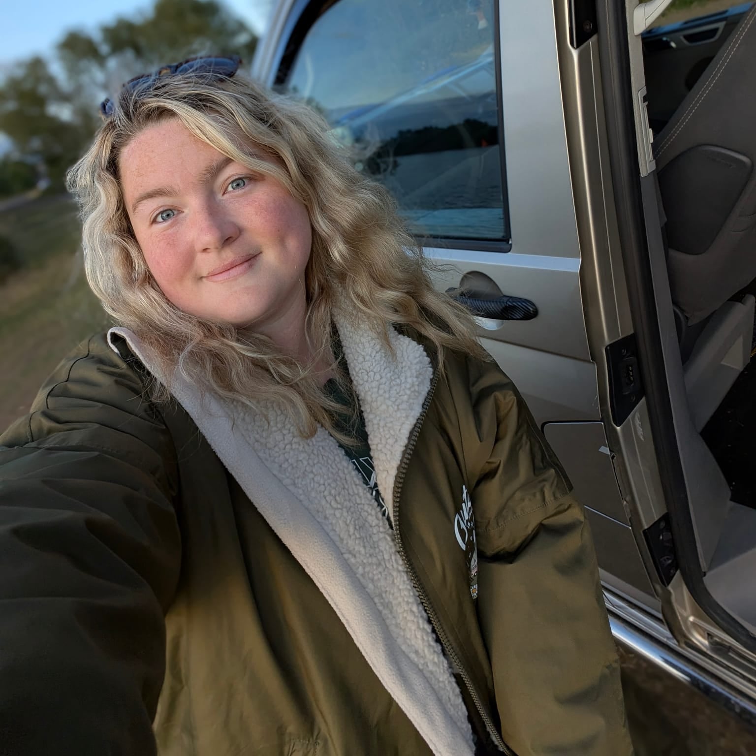 Person taking a selfie next to an open car door with a scenic background