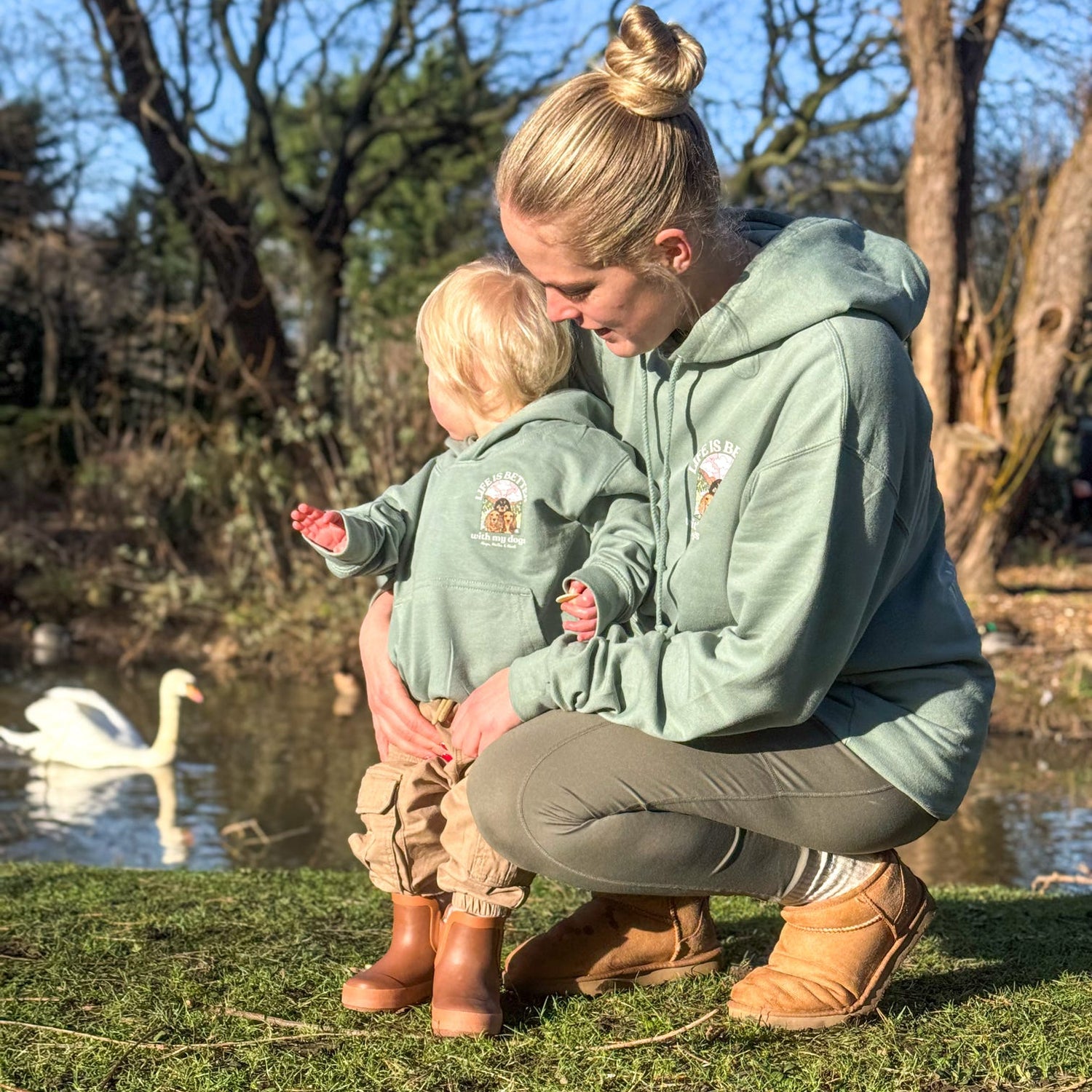 Woman and child in matching outfits by a pond with swans