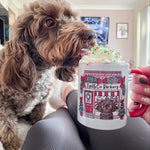 Dog drinking from a mug with a festive design held by a person indoors.