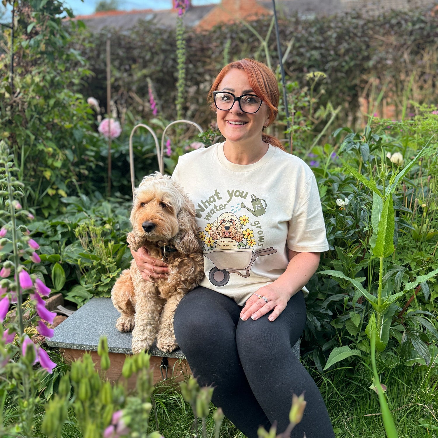Woman sitting in a garden with a dog, wearing a t-shirt with a graphic design.