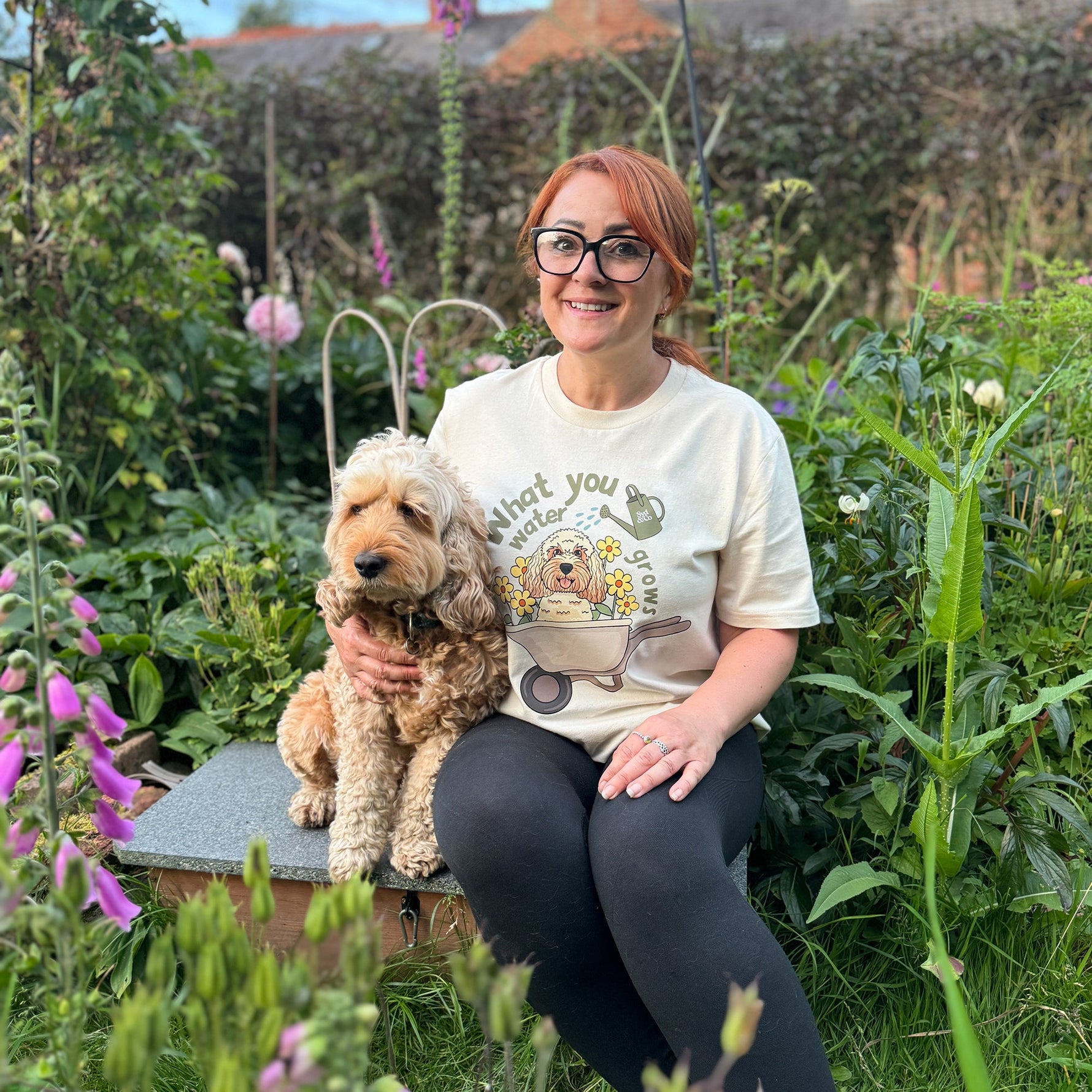 Woman sitting in a garden with a dog, wearing a t-shirt with a graphic design.